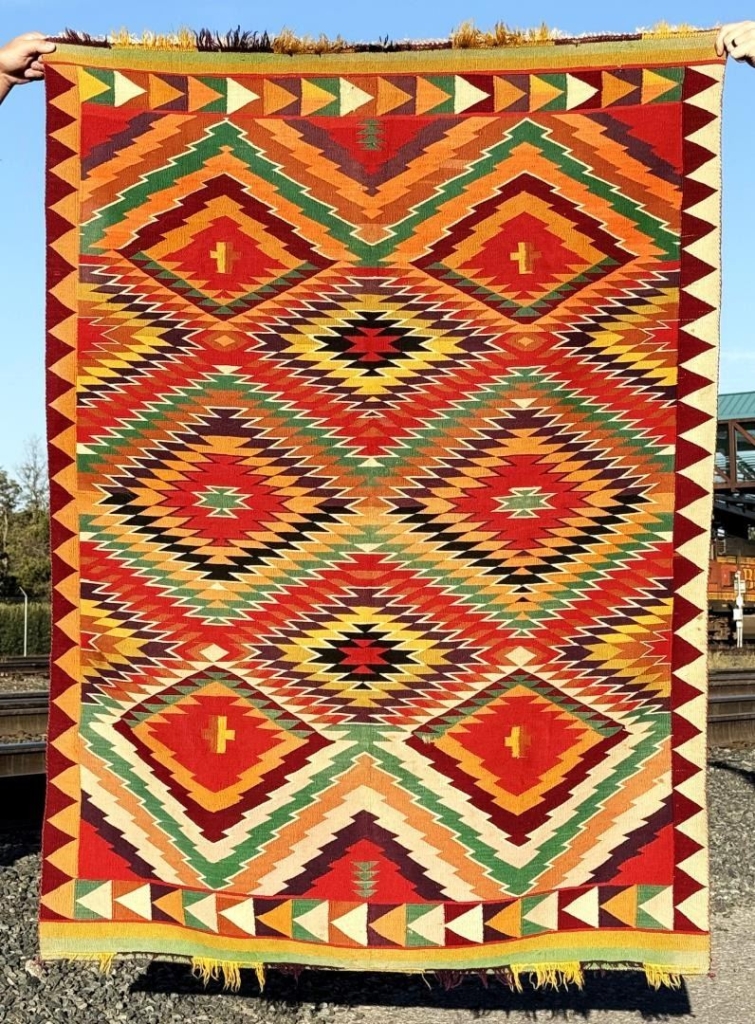 Exceptional Navajo Germantown blanket rug, 47.5" x 65", with bold geometric patterns, vibrant colors, and minor moth damage and staining.